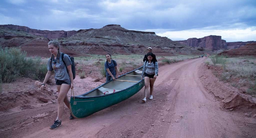 a group of three students carry a canoe on an outward bound trip in the southwest